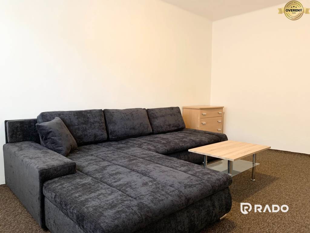 Obývacia izba v 2-izbovom byte s úplne novým veľkým gaučom, konferenčným stolíkom a komodou