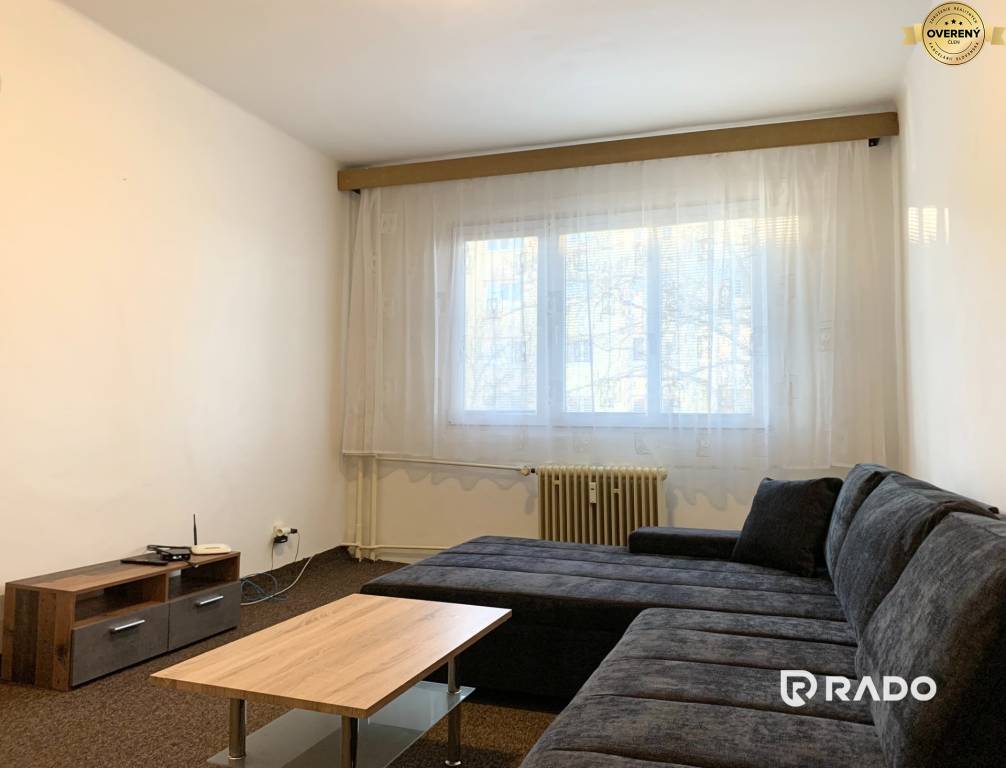 Obývacia izba v 2-izbovom byte s úplne novým veľkým gaučom, konferenčným stolíkom a skrinkou pod TV